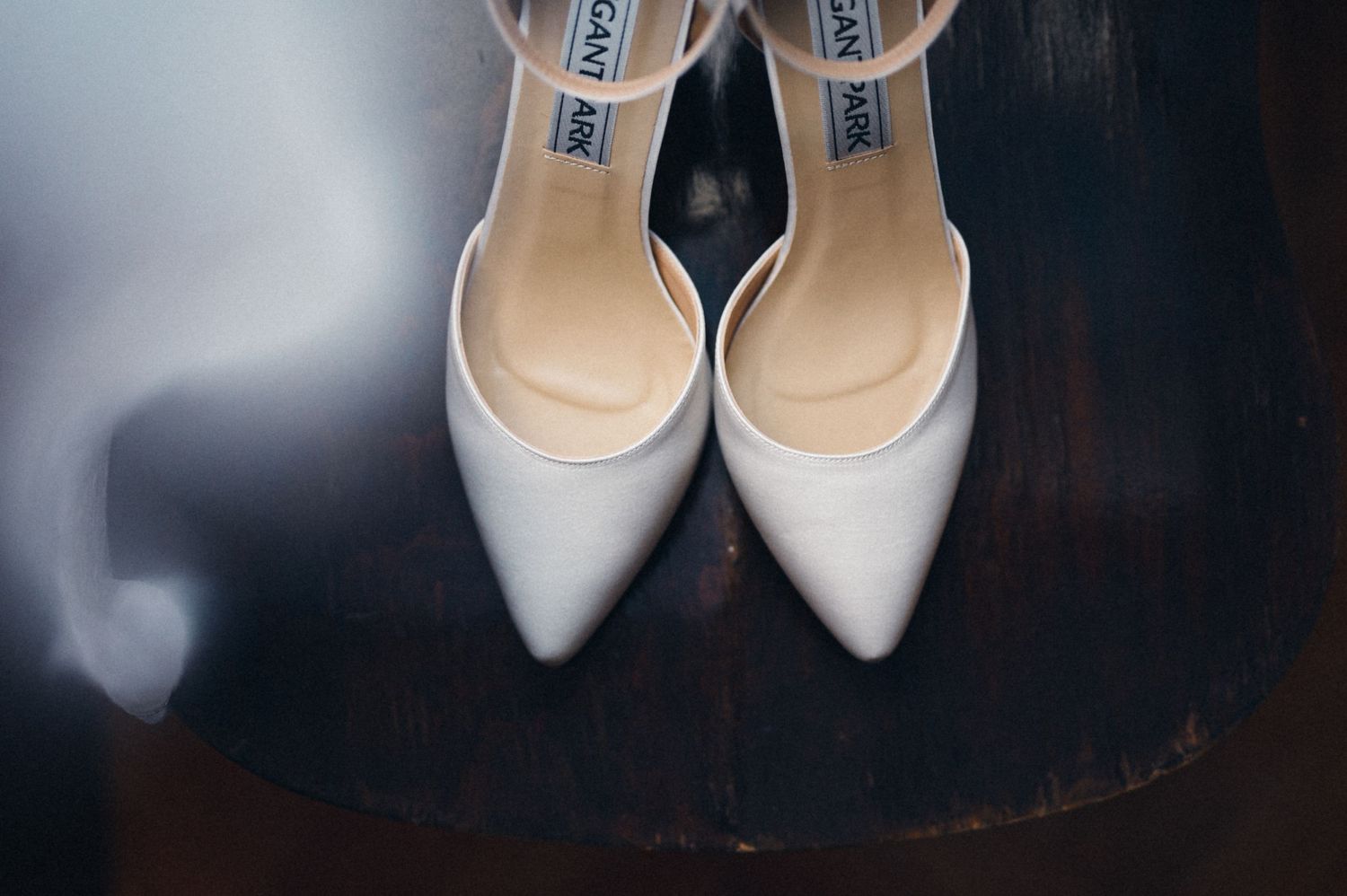 Elegant white Jimmy Choo bridal shoes on dark wooden surface.