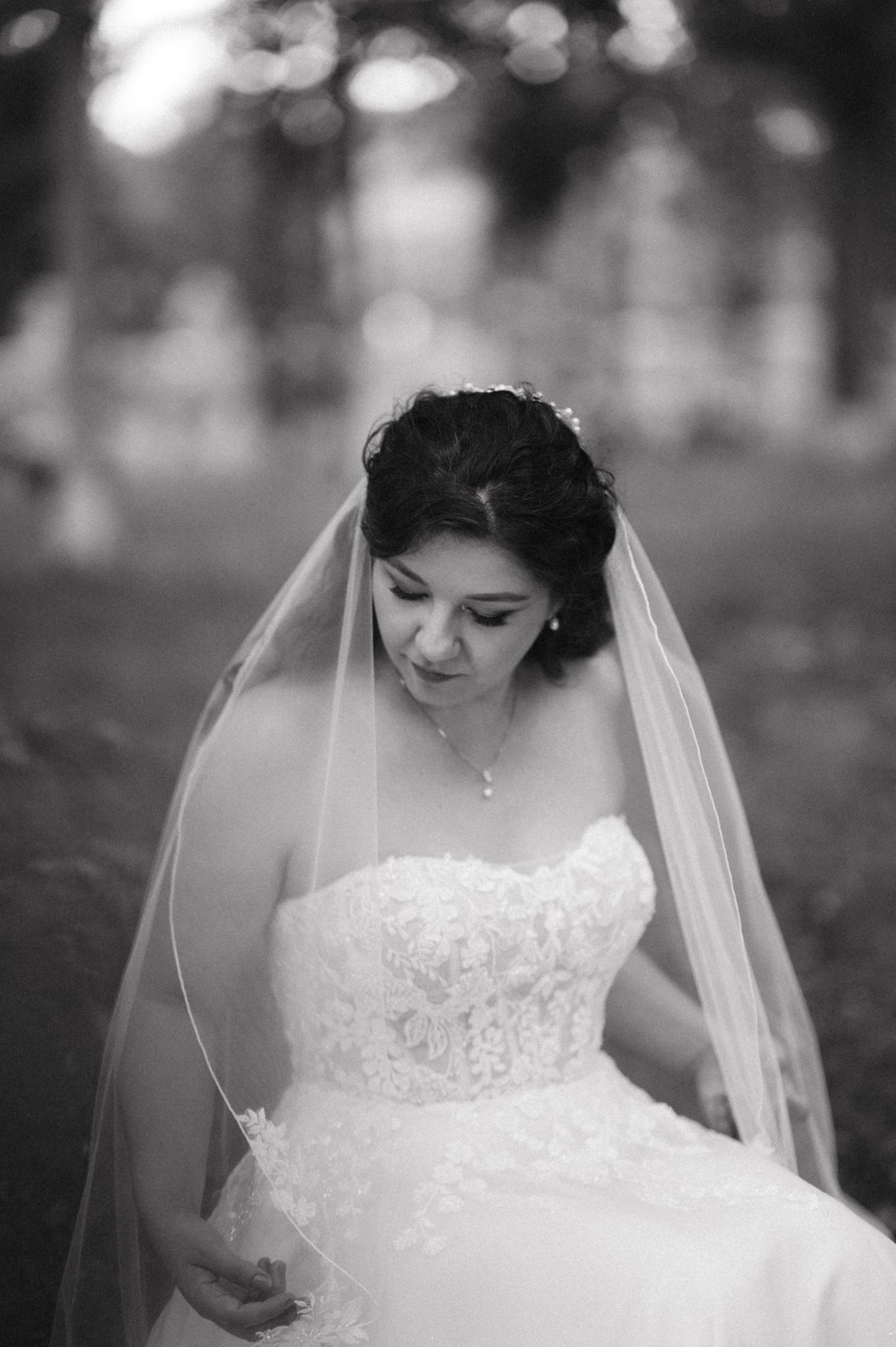 A bride wearing a white lace wedding dress and veil in black and white portrait style.