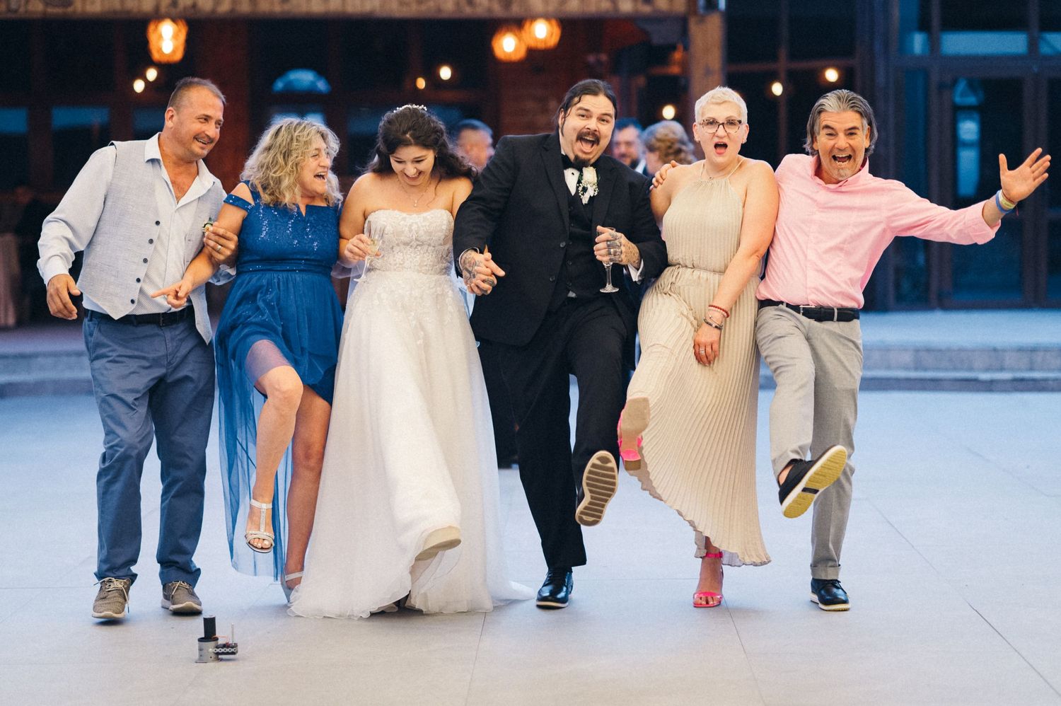 Wedding party friends dancing and jumping together on a dance floor during reception celebrations.