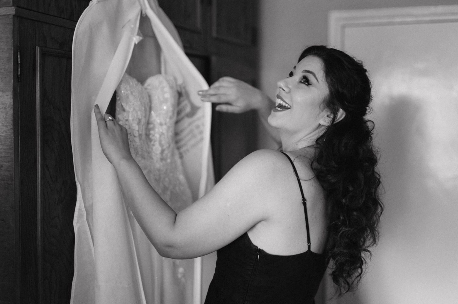 Black and white photo of someone with long curly hair handling a wedding dress.