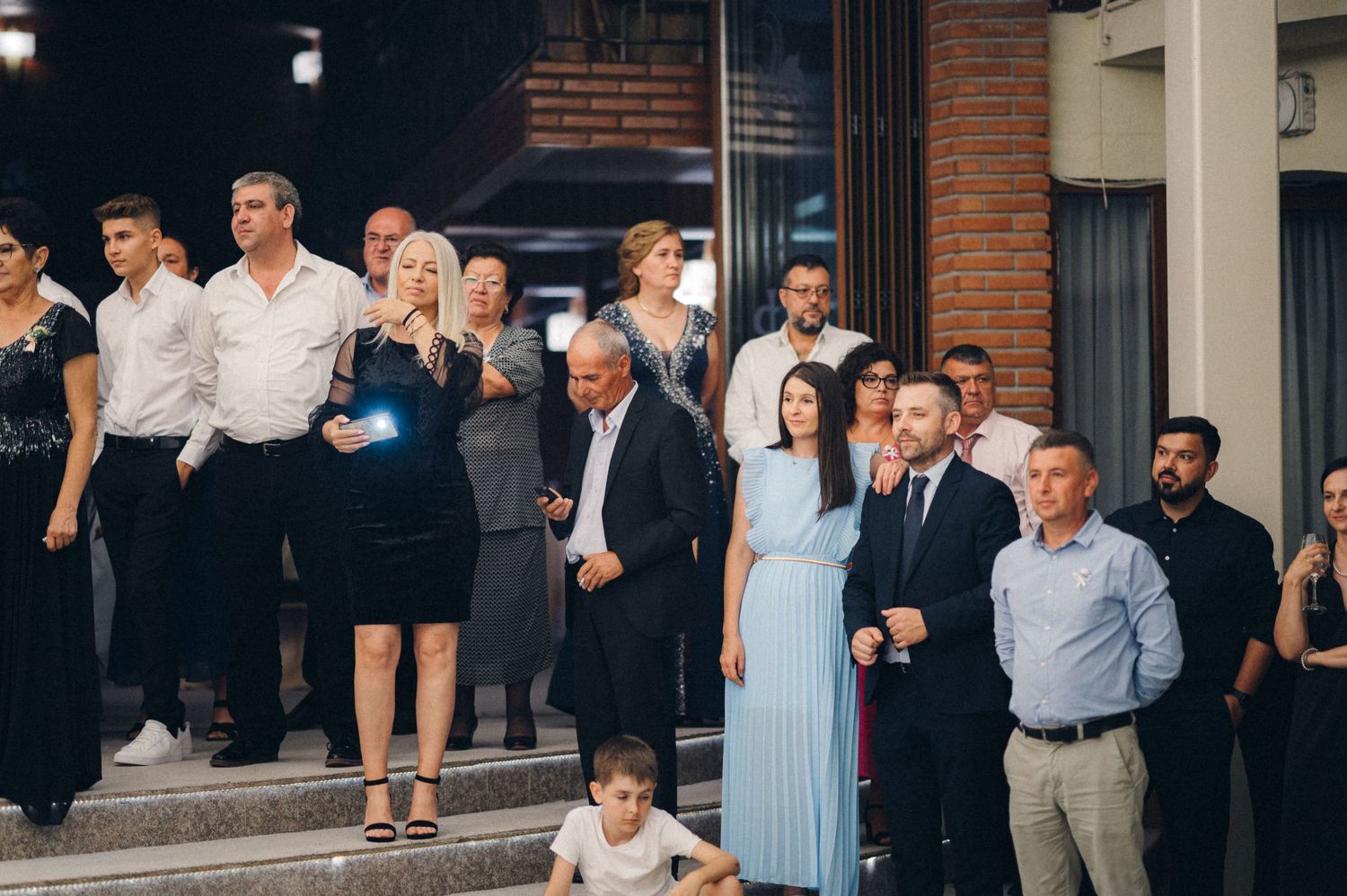 Group of formally dressed guests gathered outside a venue at an elegant event.