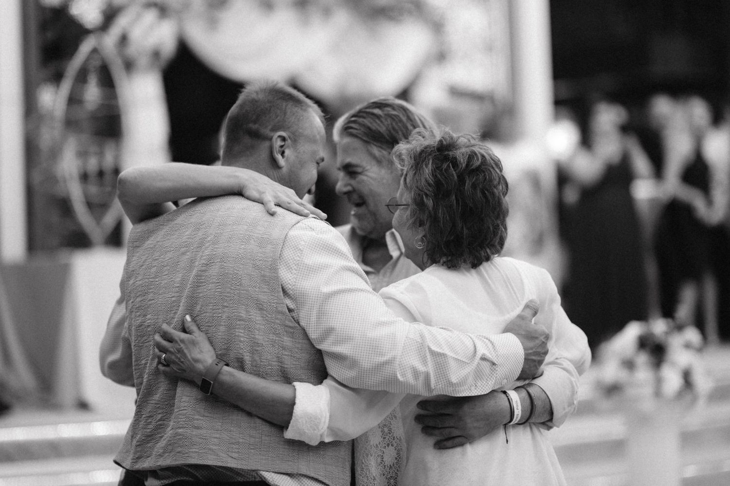 Three people share a joyful group hug in black and white photography.