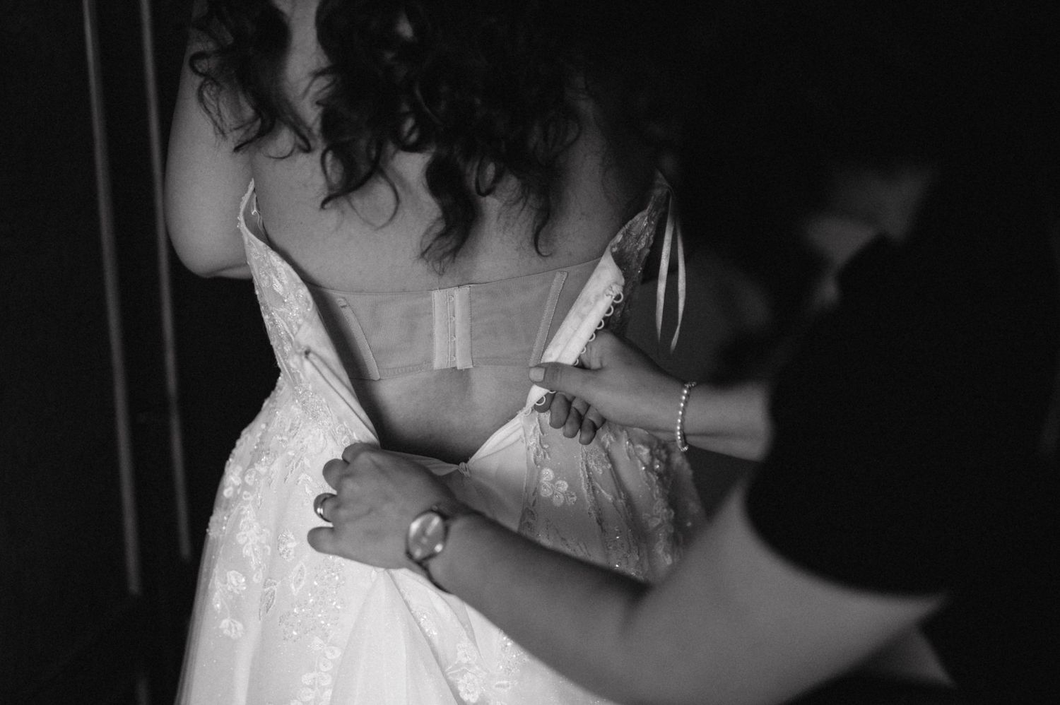 Black and white image showing details of a wedding dress being adjusted.