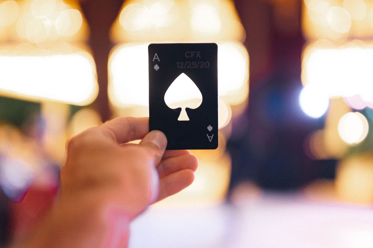 Close-up of a hand holding the ace of spades playing card against blurred lights.