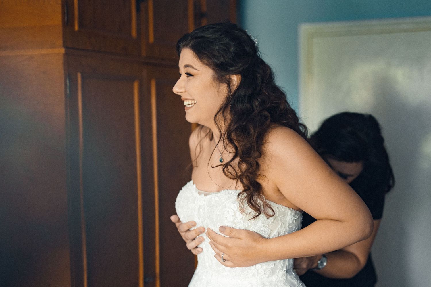 Getting ready scene showing the delicate process of adjusting a white wedding gown.