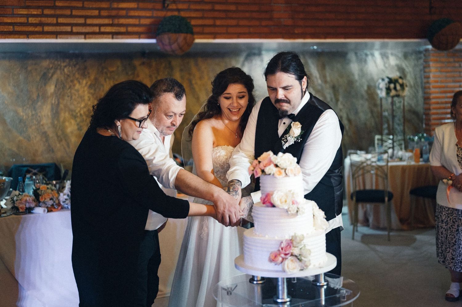 Wedding party gathers around to cut the decorative tiered cake together.