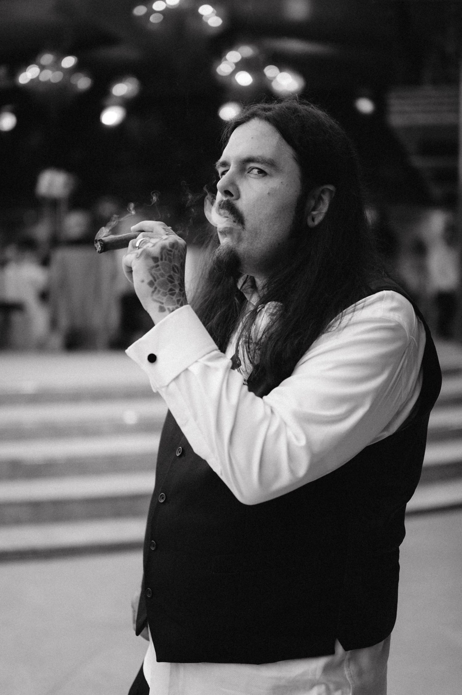 Figure in formal attire smoking while standing indoors under dim lighting.