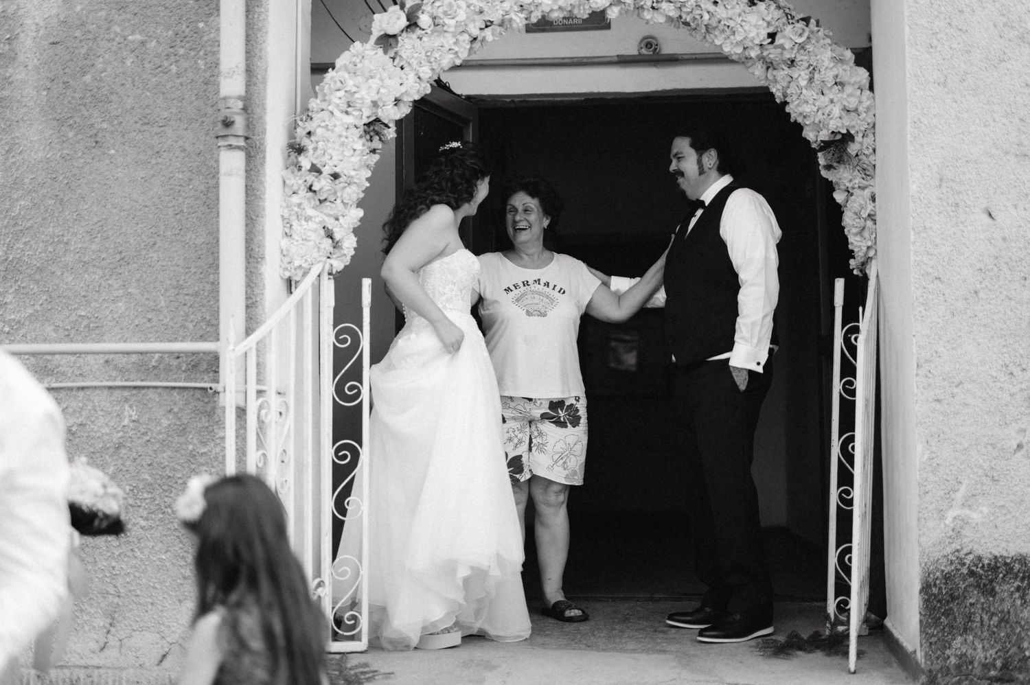 A joyful wedding celebration moment under a floral arch decorated with white flowers.