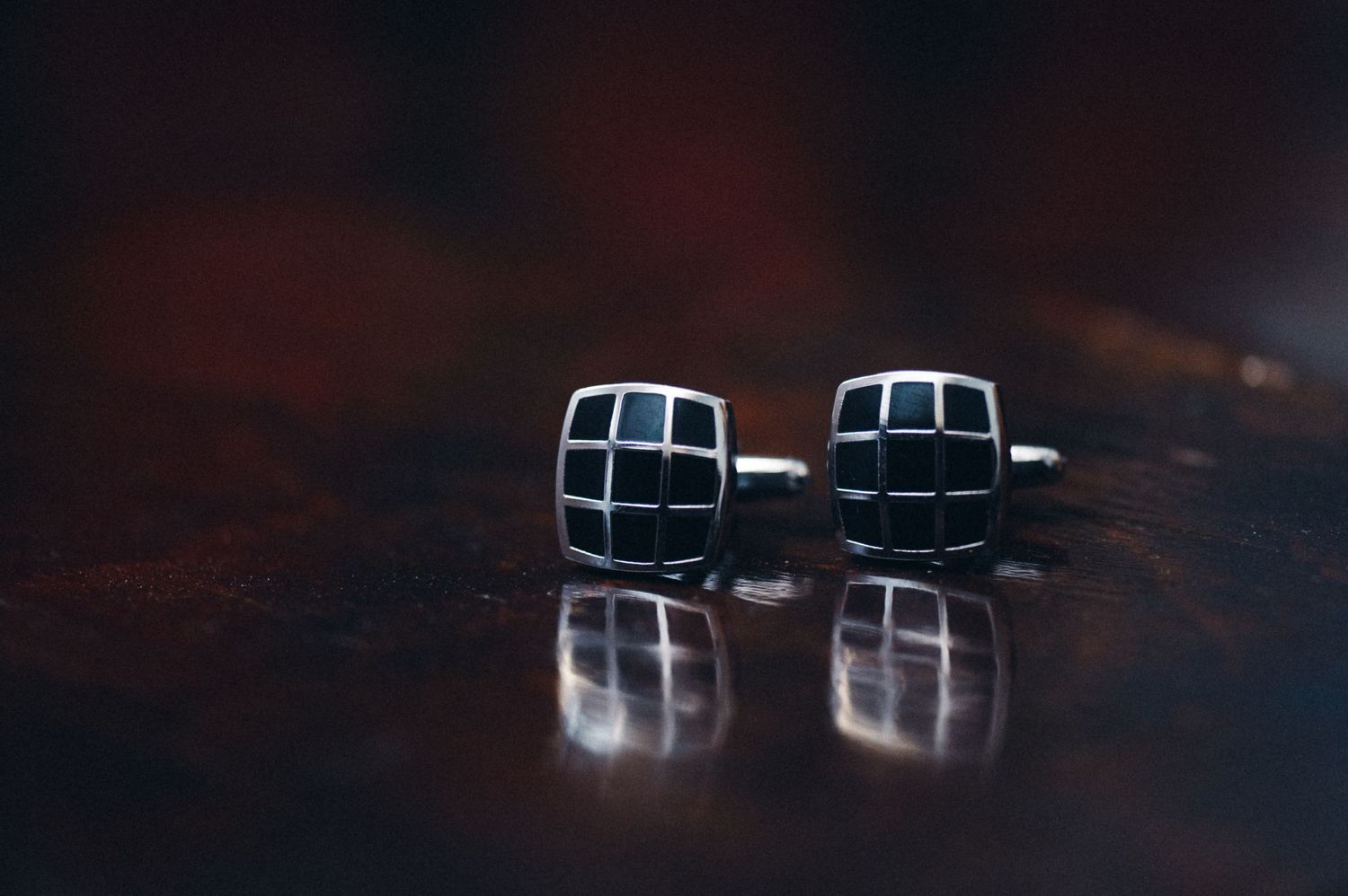 Elegant black and silver checkered cufflinks reflecting on a dark glossy surface.