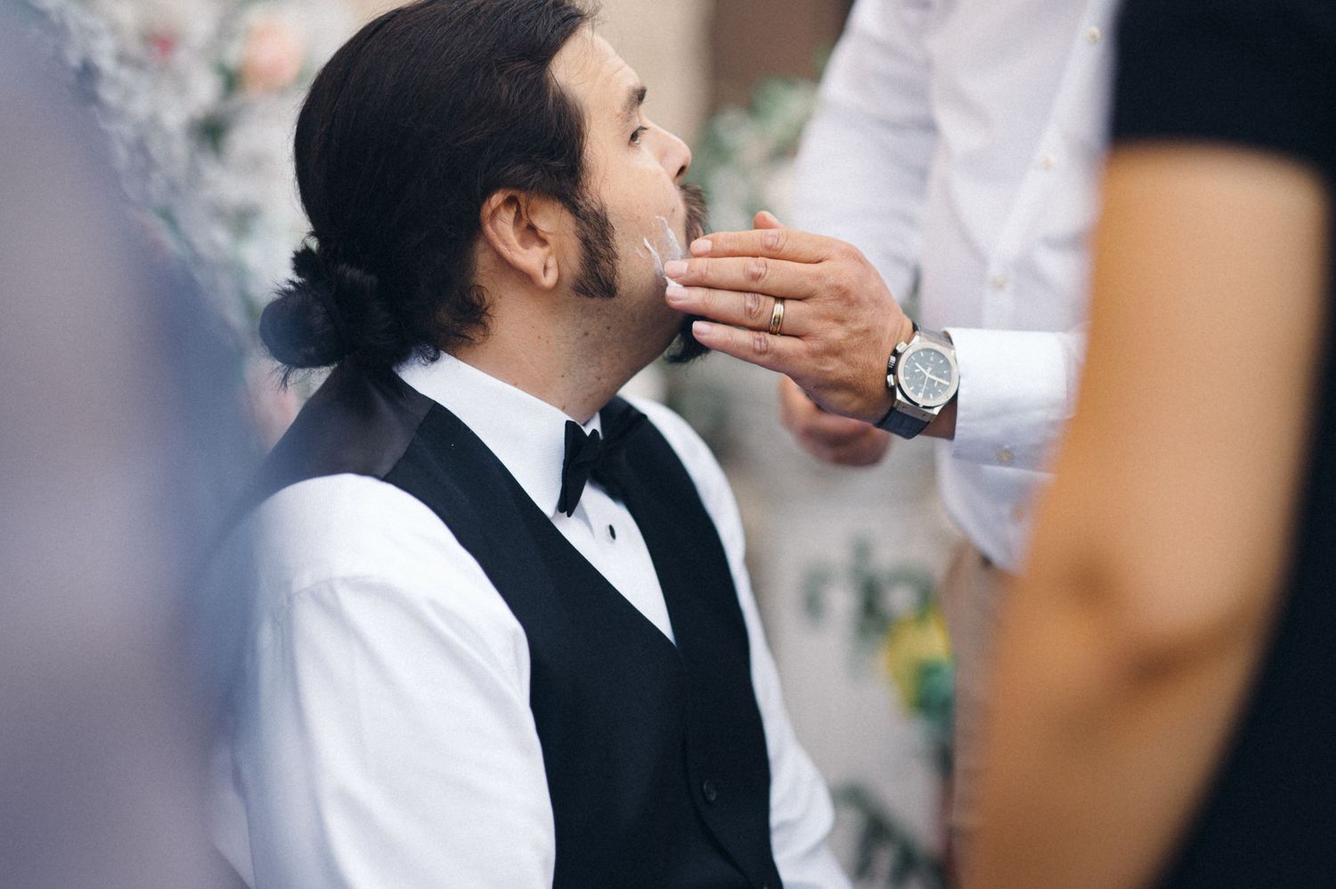 Someone in formal attire being pampered during a wedding preparation.