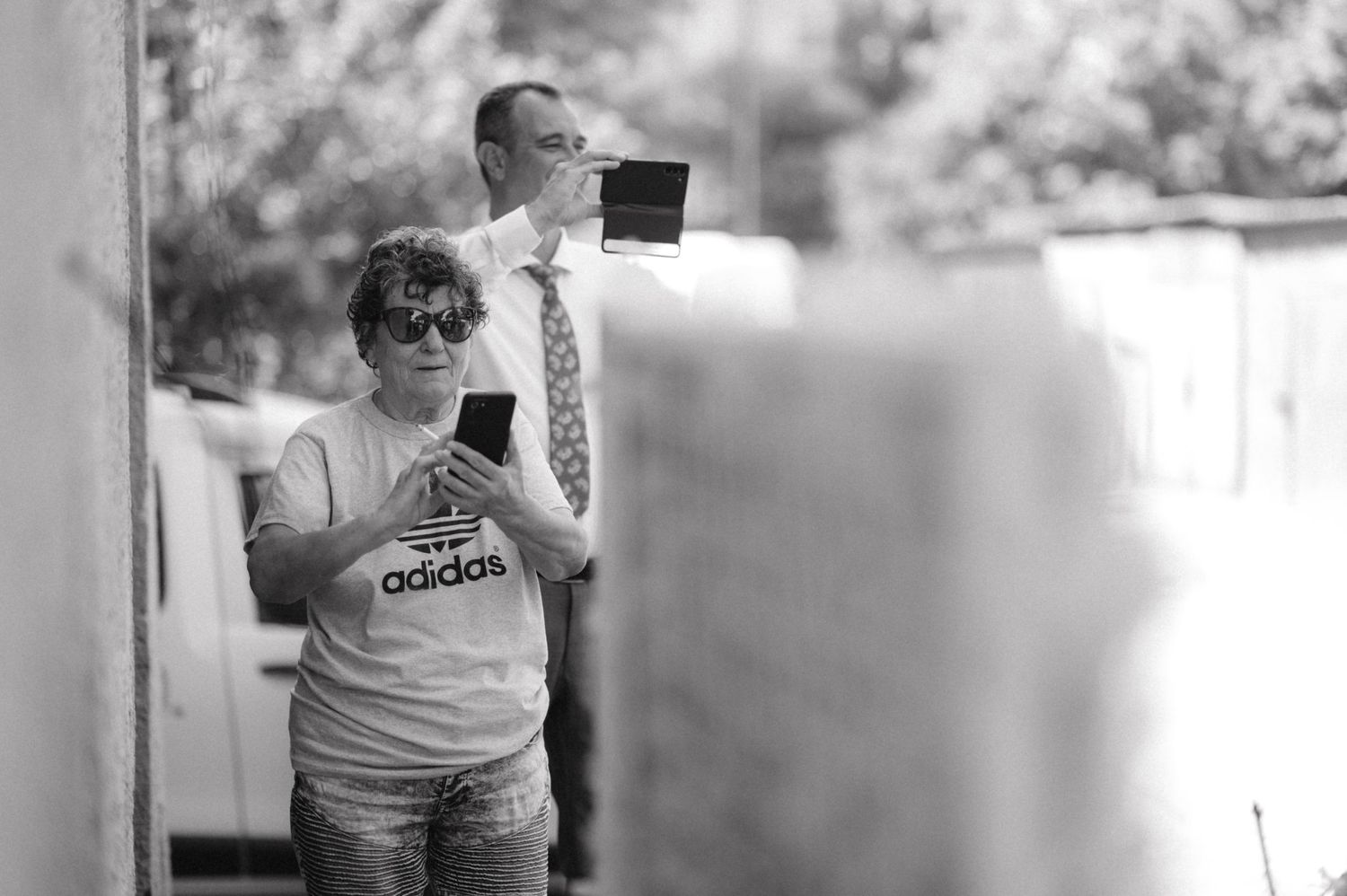 Two people holding phones up to photograph something outdoors.