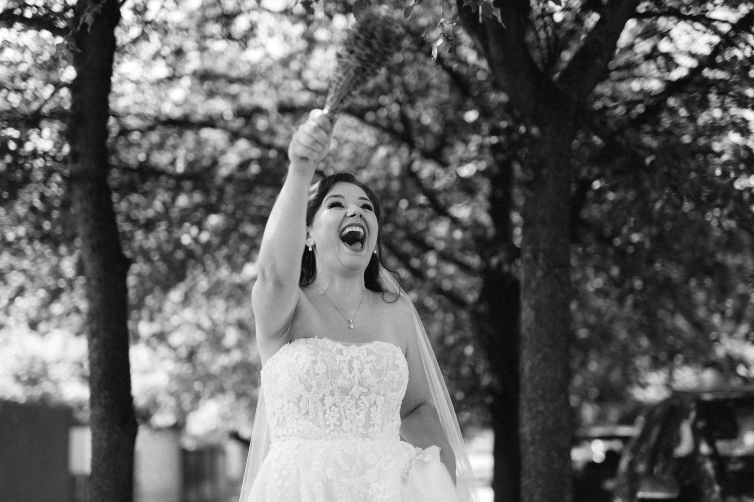 Black and white photo of joyful moment in wedding dress with arms raised.