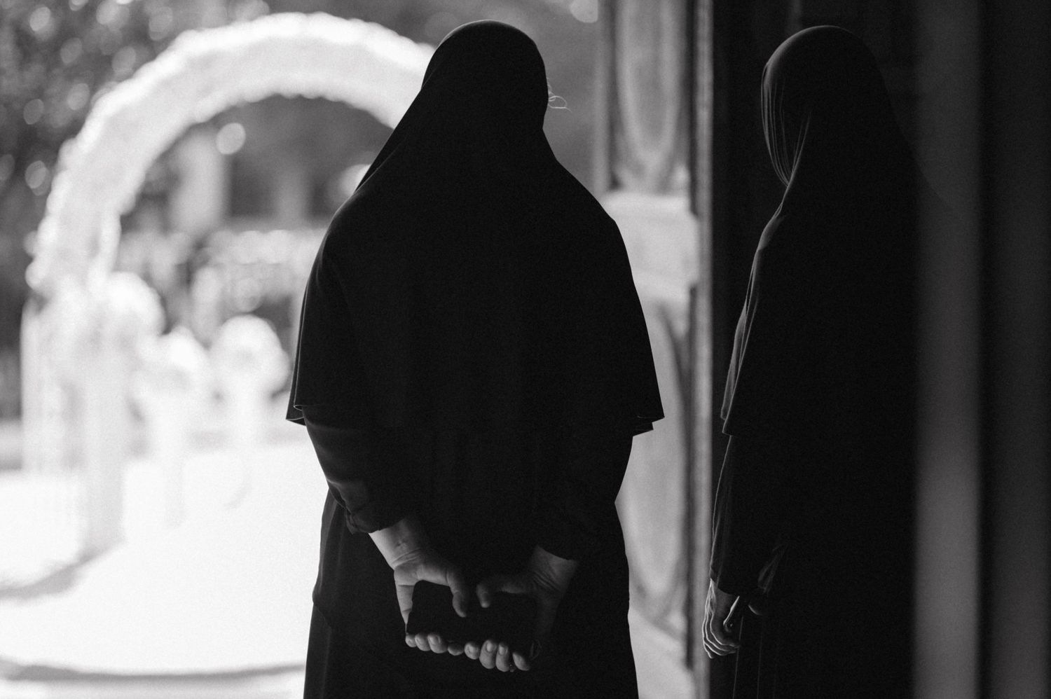 Silhouettes of two people in traditional religious garments against bright background.
