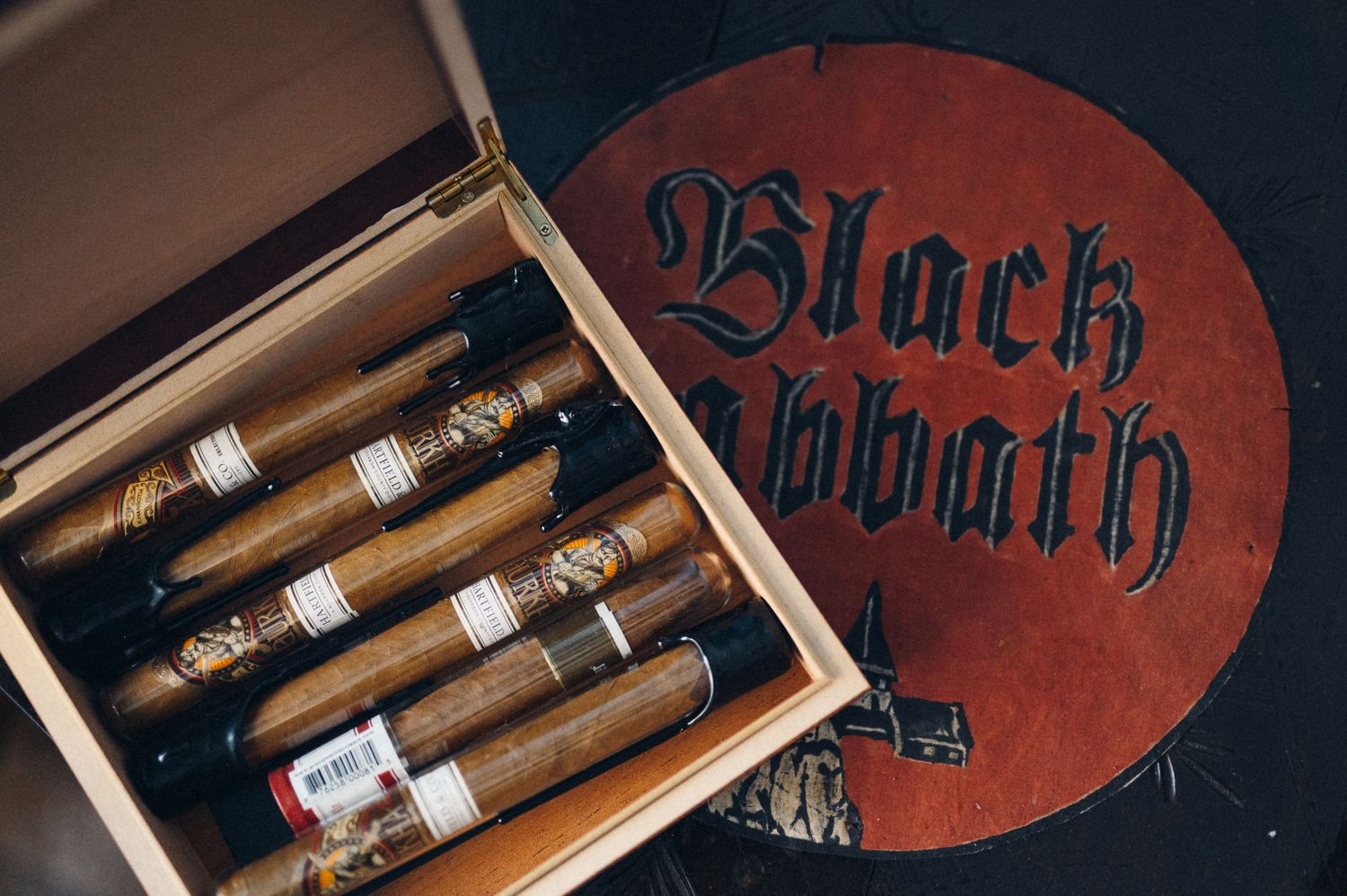 Wooden box filled with cigars and Black Bbath logo on red background.