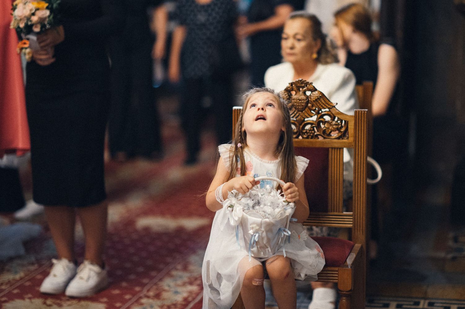 Young child in formal dress sitting on ornate wooden chair during wedding ceremony.