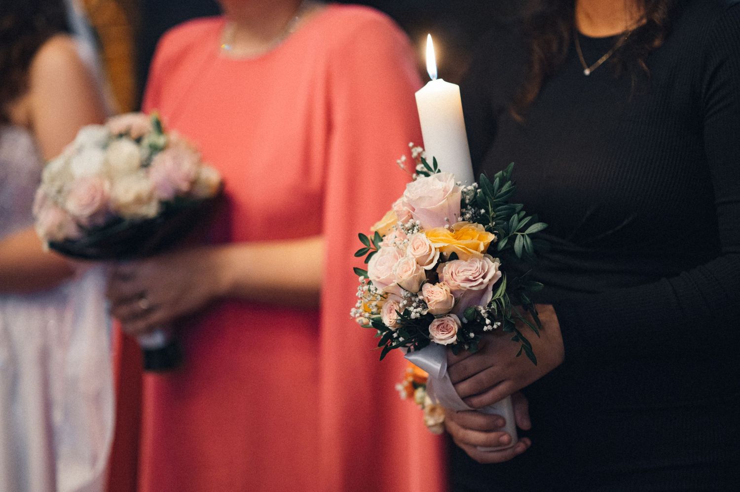 Close-up of hands holding bouquet and candle during wedding ceremony.