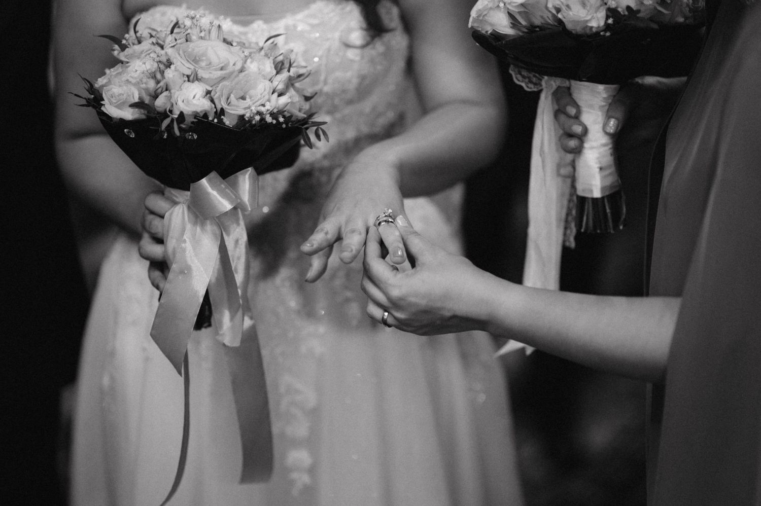 A close-up black and white photo showing hands adjusting a white wedding dress detail.