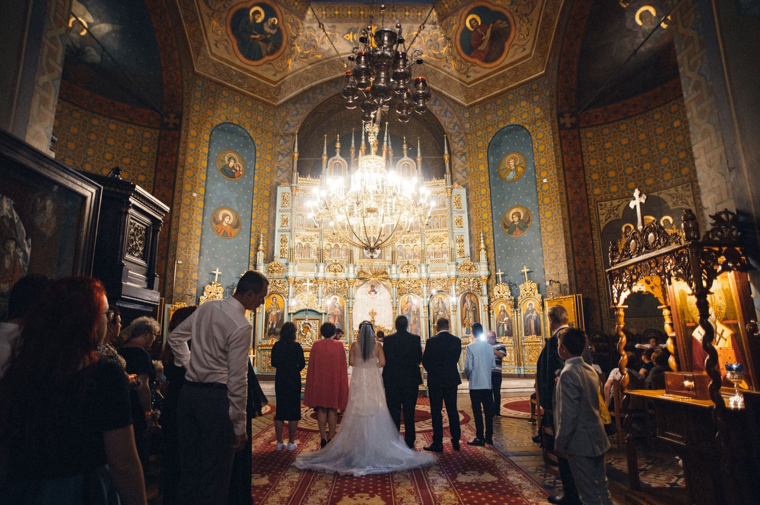 Ornate orthodox church interior with chandelier during a wedding ceremony.