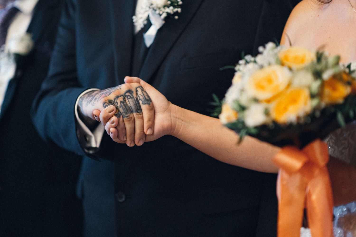 Close-up of hands exchanging rings with yellow bouquet in background.