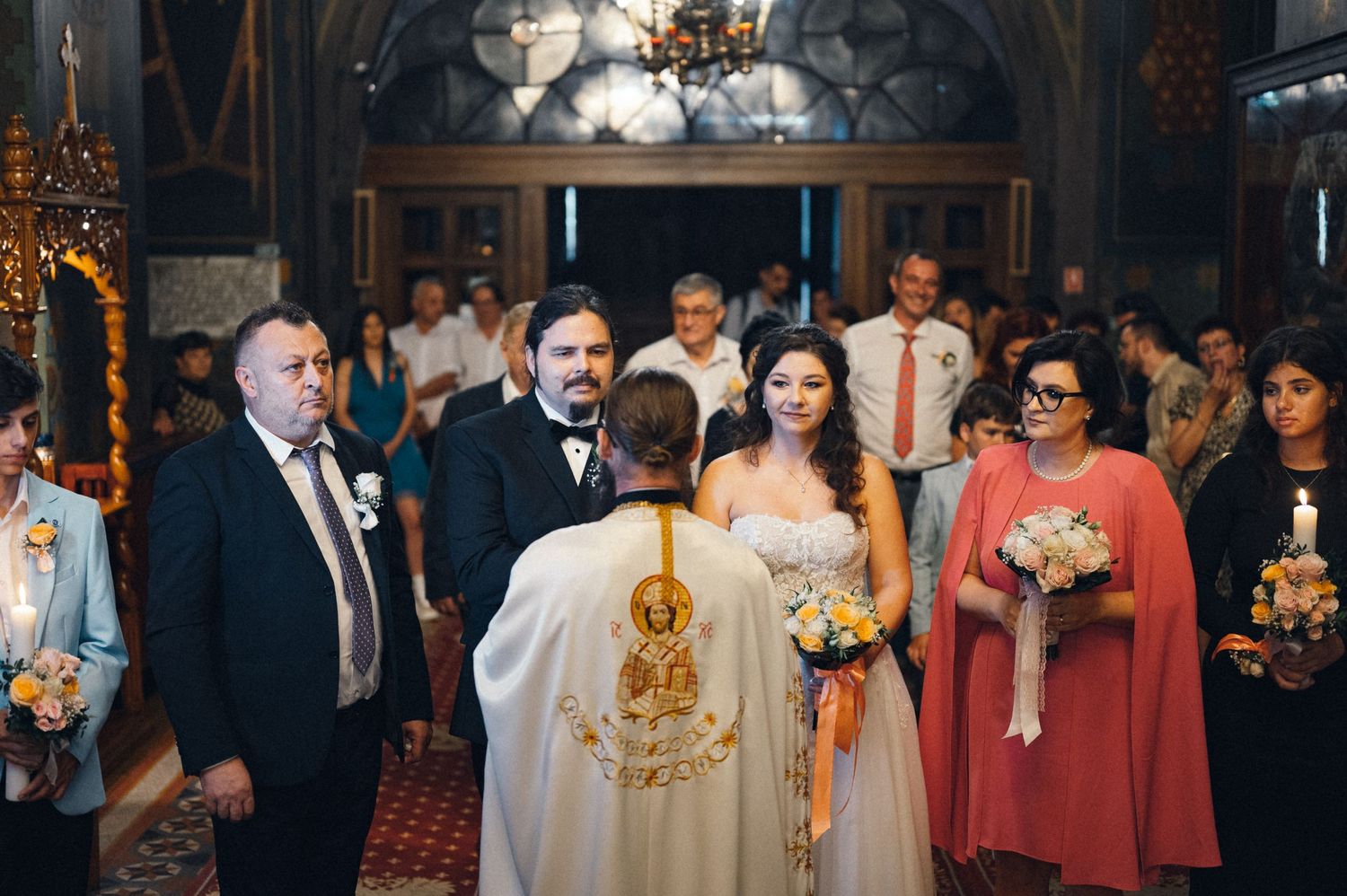Orthodox wedding ceremony with priest and attendees in an ornate church setting.