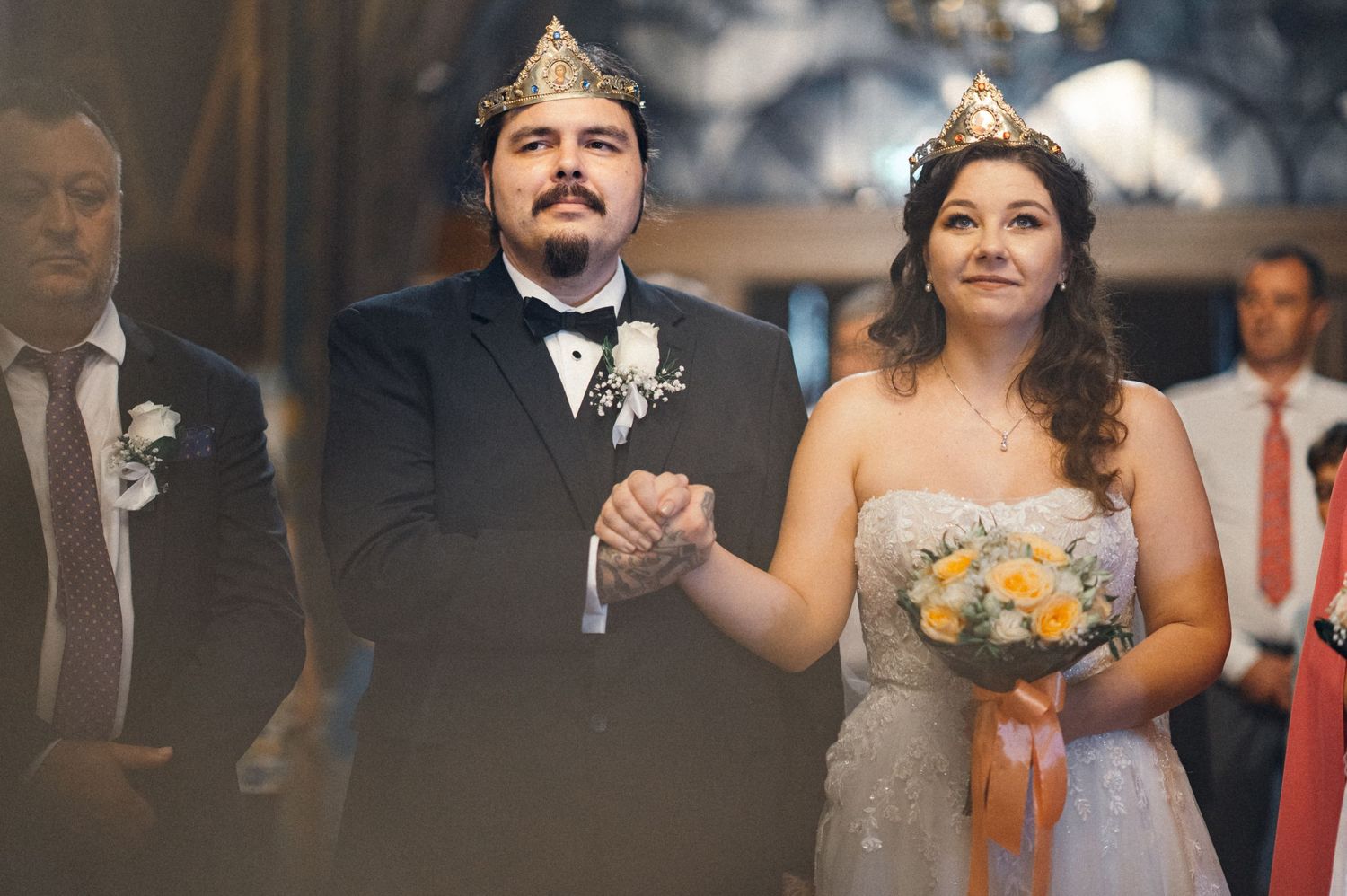 A couple stands together during their Orthodox wedding ceremony wearing crowns.