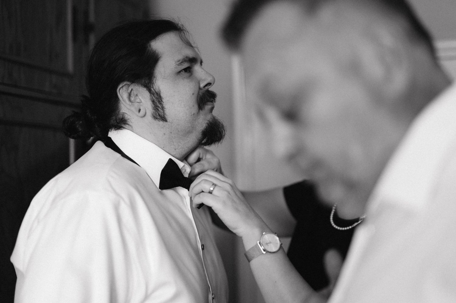 Black and white image of someone adjusting their bowtie before an event.