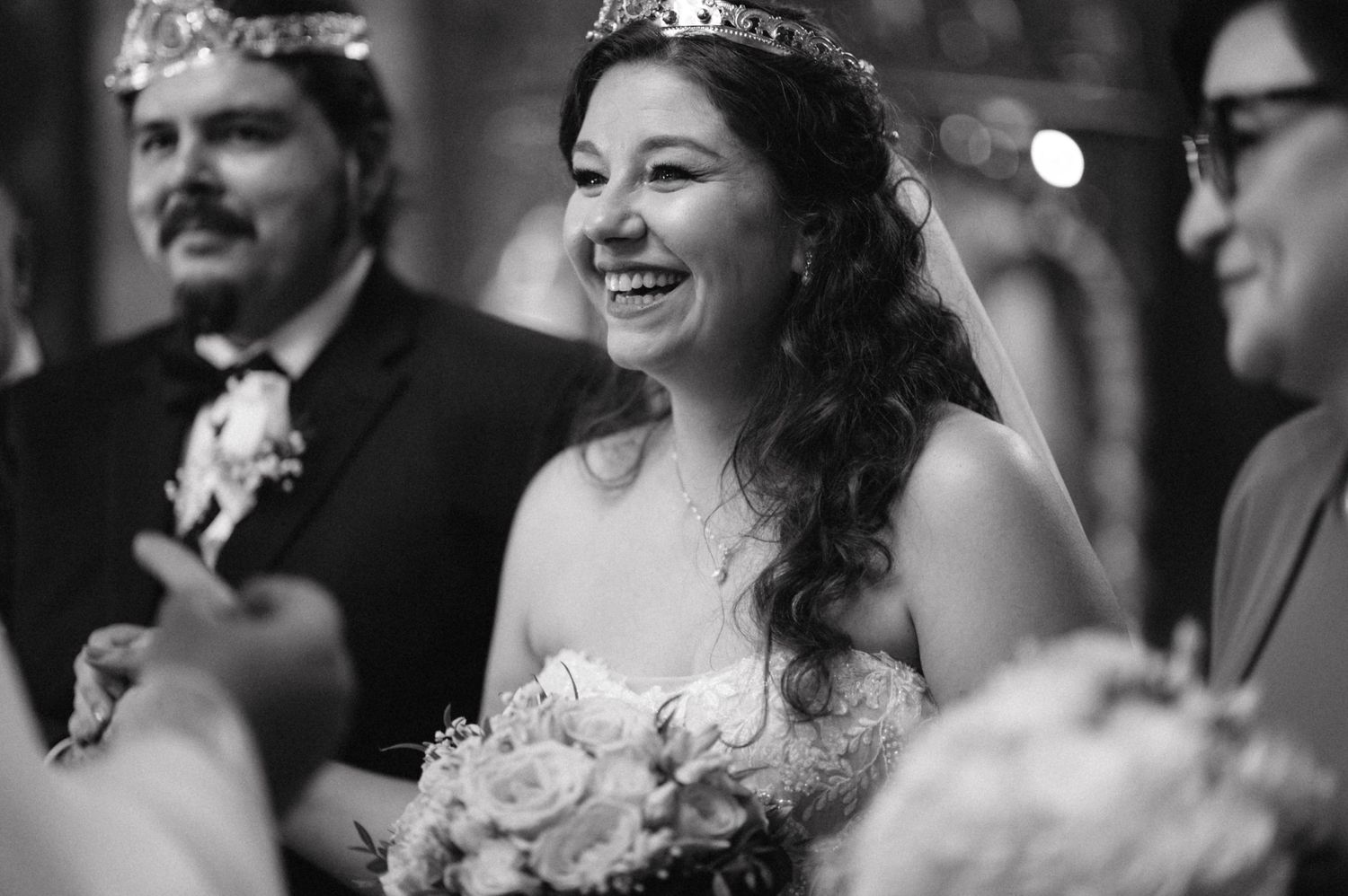 A bride wearing a tiara and holding flowers smiles during her wedding ceremony.