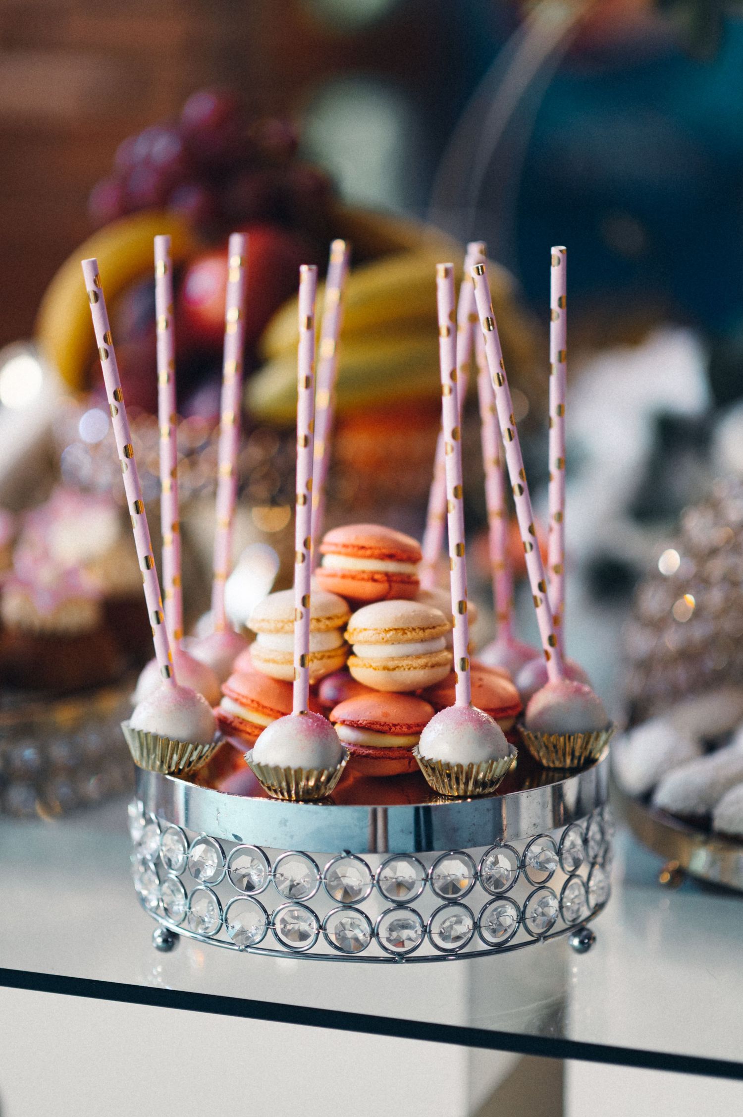 Elegant display of macarons and cake pops on crystal stand for wedding dessert table.