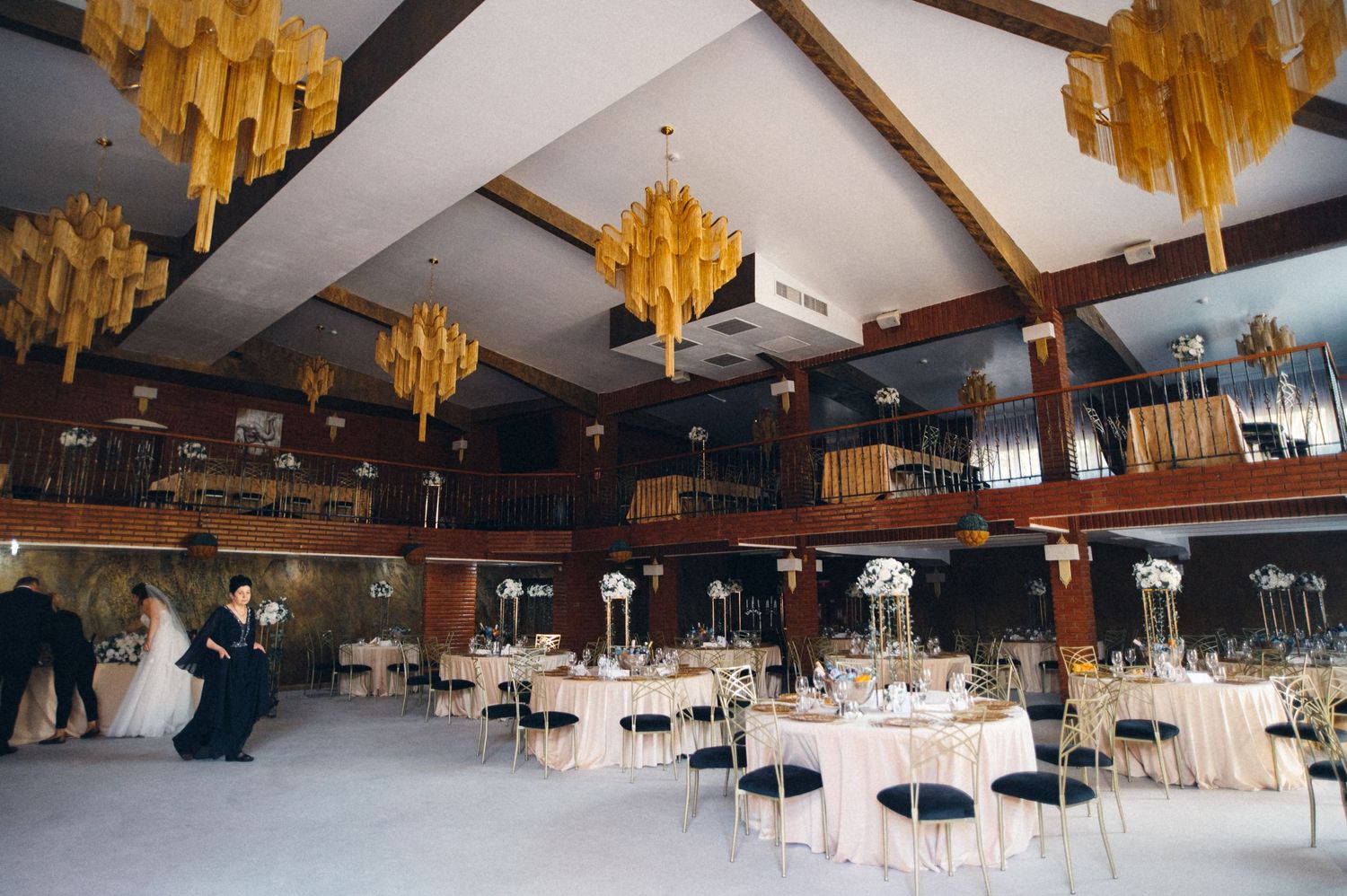 Large event venue with yellow chandeliers and white tables set for a wedding reception.