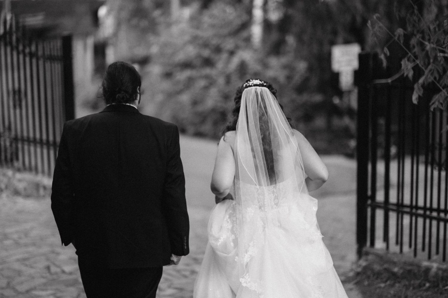 Back view of newlyweds walking down path near iron fence.