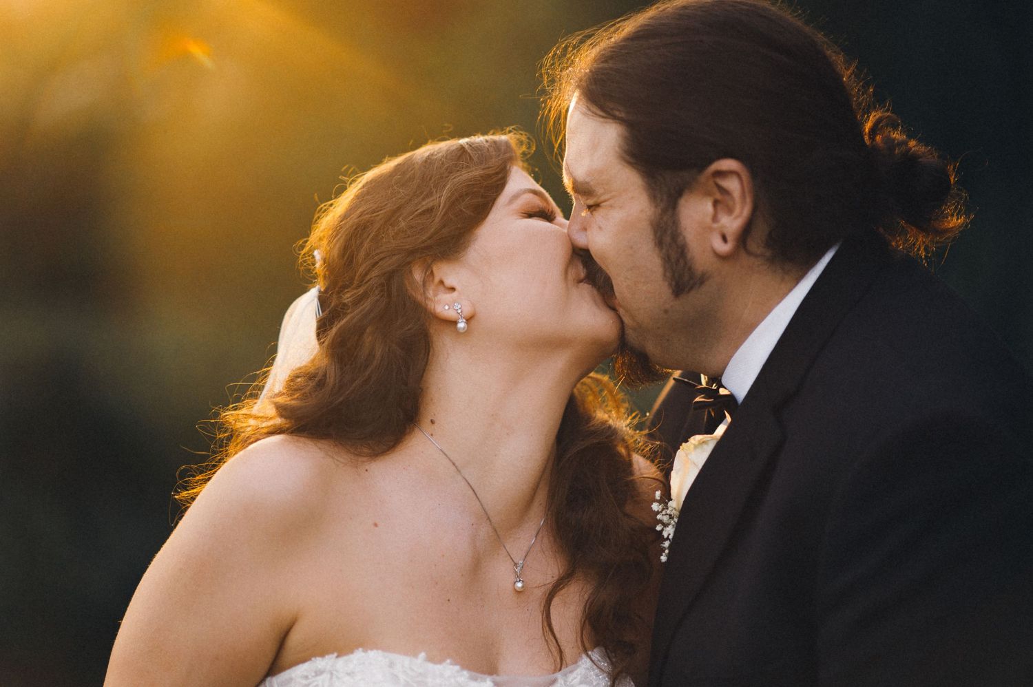 A romantic wedding couple shares a kiss at sunset with golden light illuminating the intimate moment.