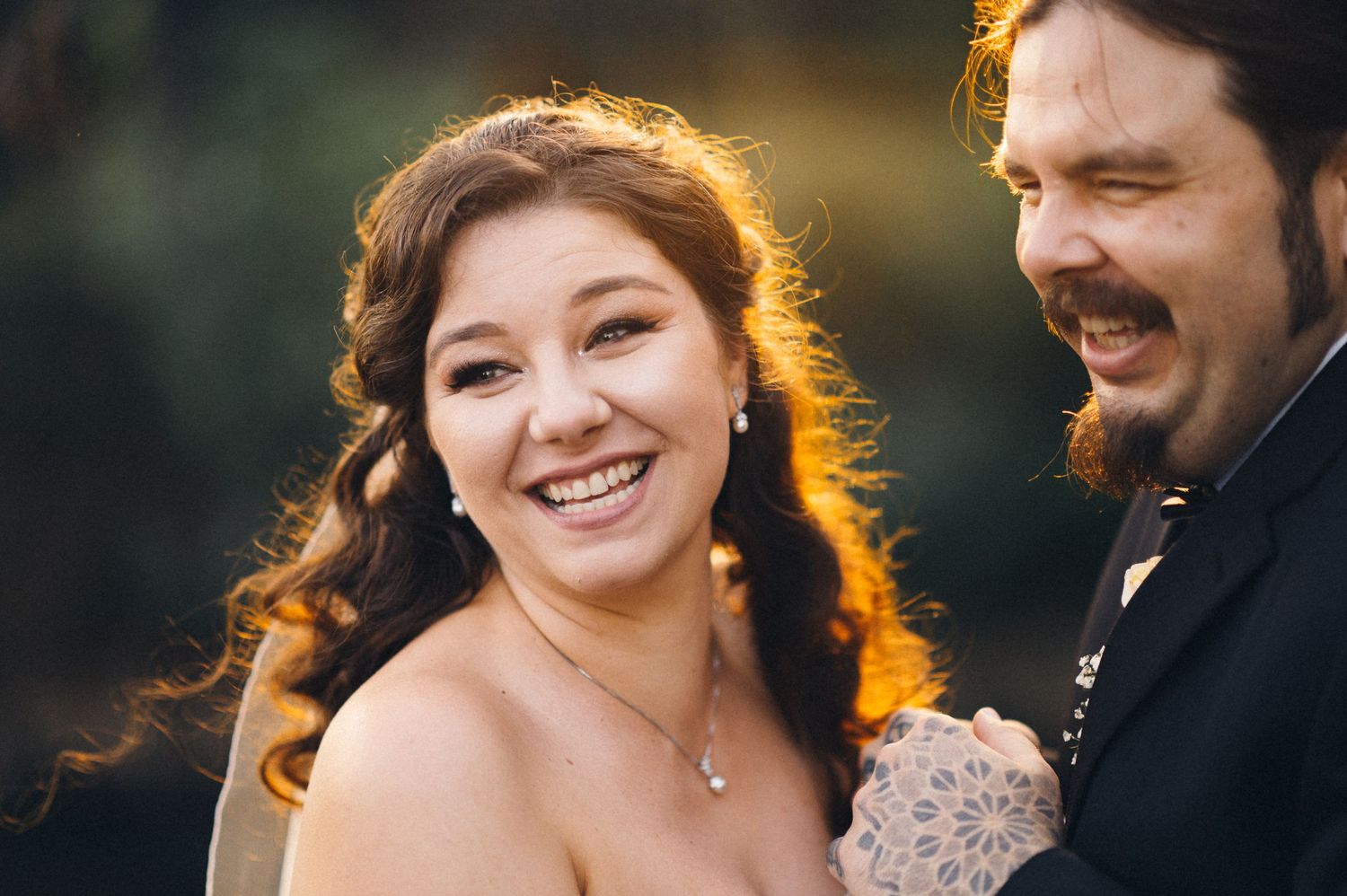 A backlit wedding portrait captures a loving candid moment between newlyweds at sunset.