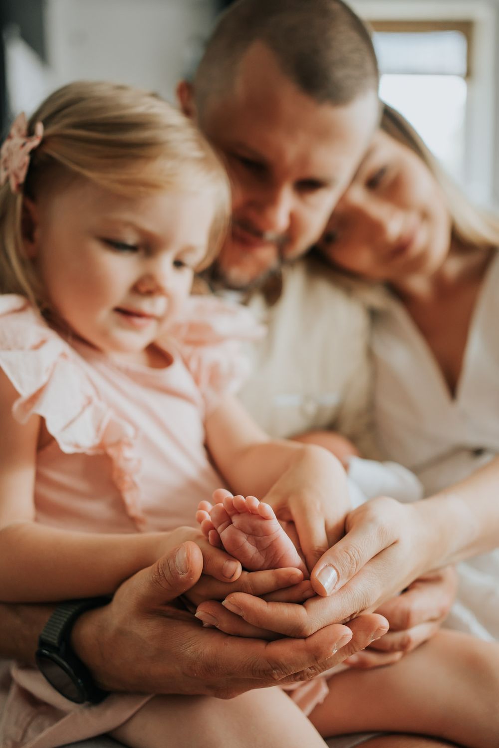 Starsza siostra, mama i tata trzymają stópki noworodka - sesja rodzinna Kraków