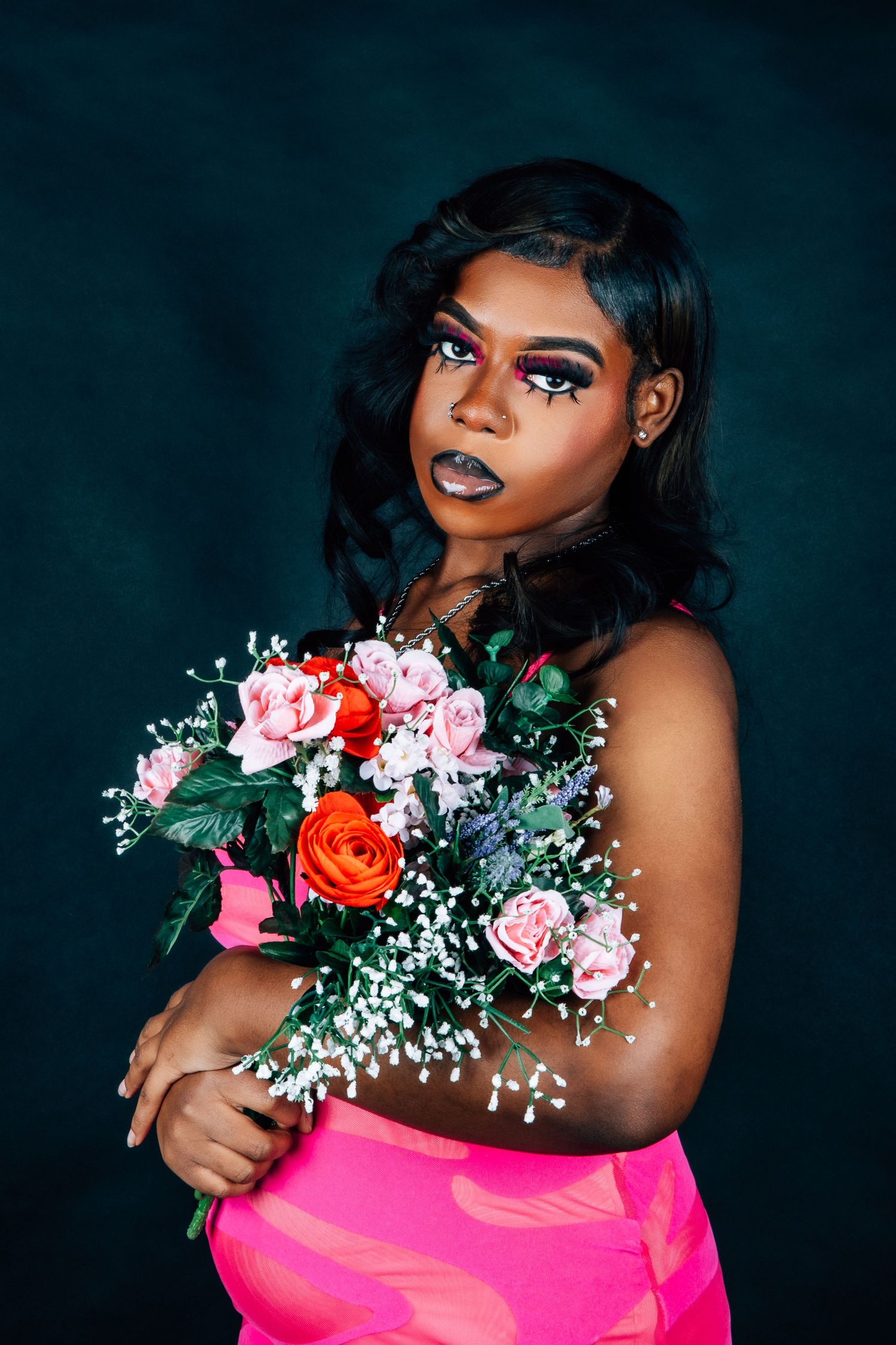 Fashion portrait with model in pink dress holding colorful bouquet against dark teal background.