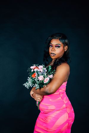 Dramatic fashion photo with model in bright pink dress holding floral arrangement.