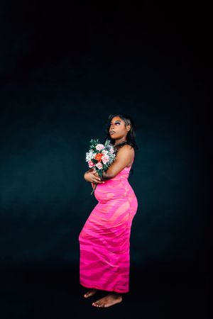 Artistic portrait series featuring pink satin dress and fresh flower bouquet against dark backdrop.
