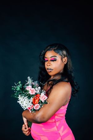Glamour portrait with dramatic makeup and pink dress holding fresh flower arrangement.