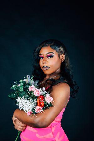 Fashion editorial style portrait with bold makeup and pink dress against dark background.