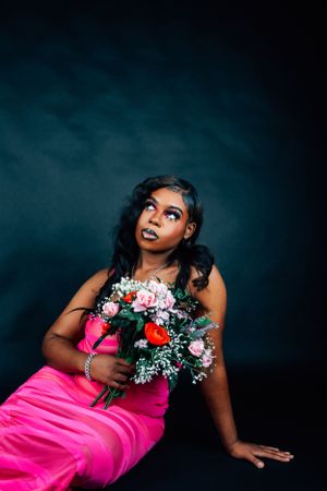 Artistic portrait with upward gaze holding vibrant flower bouquet in pink formal dress.