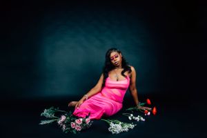 Stylish studio photo with model reclining among scattered flowers in bright pink gown.
