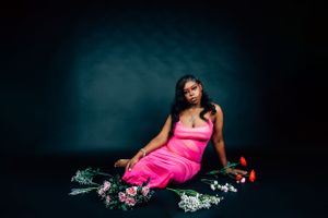 Moody fashion portrait with scattered flowers and hot pink dress against dark studio backdrop.