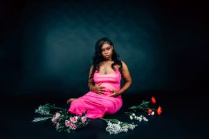 Dramatic portrait with floral elements and bright pink dress against deep teal background.