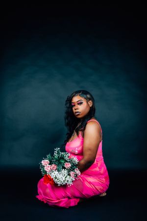Artistic fashion photograph with pink dress and floral arrangement in dark studio setting.