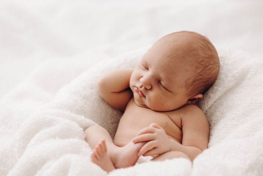 Peaceful sleeping newborn baby resting on creamy white textured bedding.