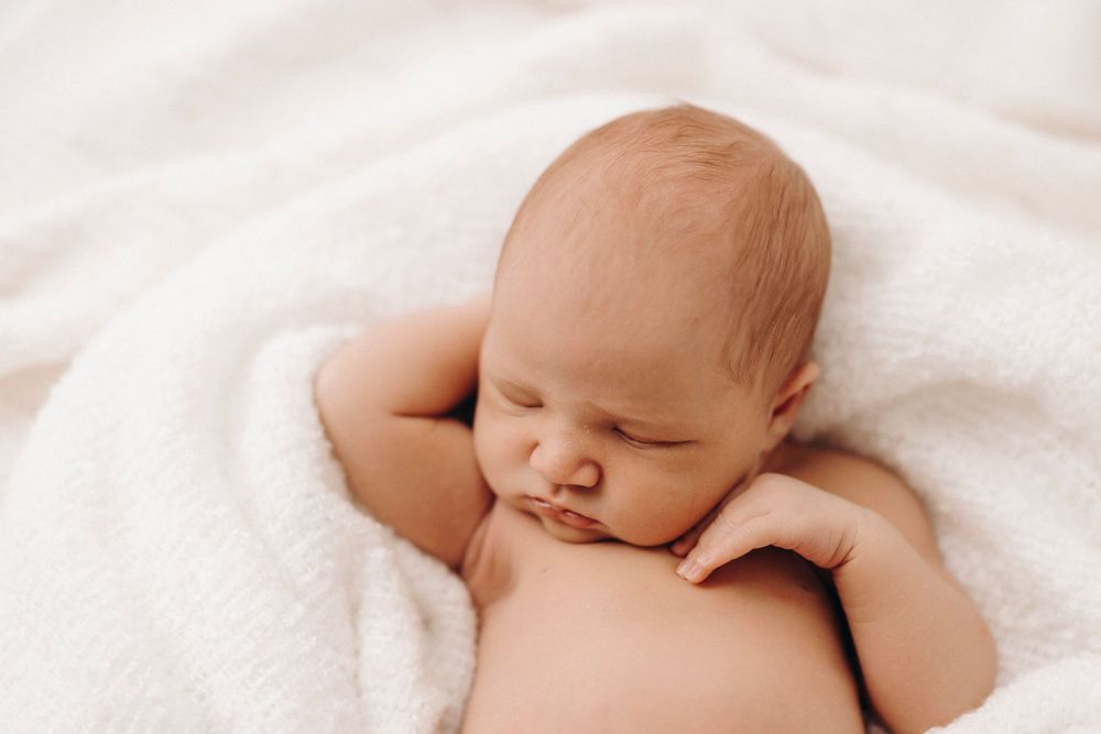 Sleeping newborn baby lying peacefully on white blanket.