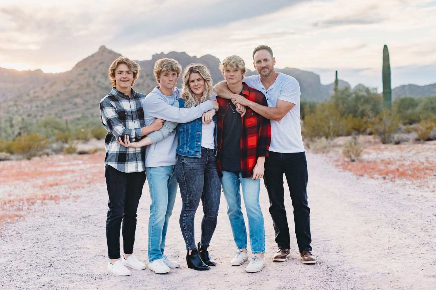 Group of friends standing together on a desert path with mountains and cacti in the background.