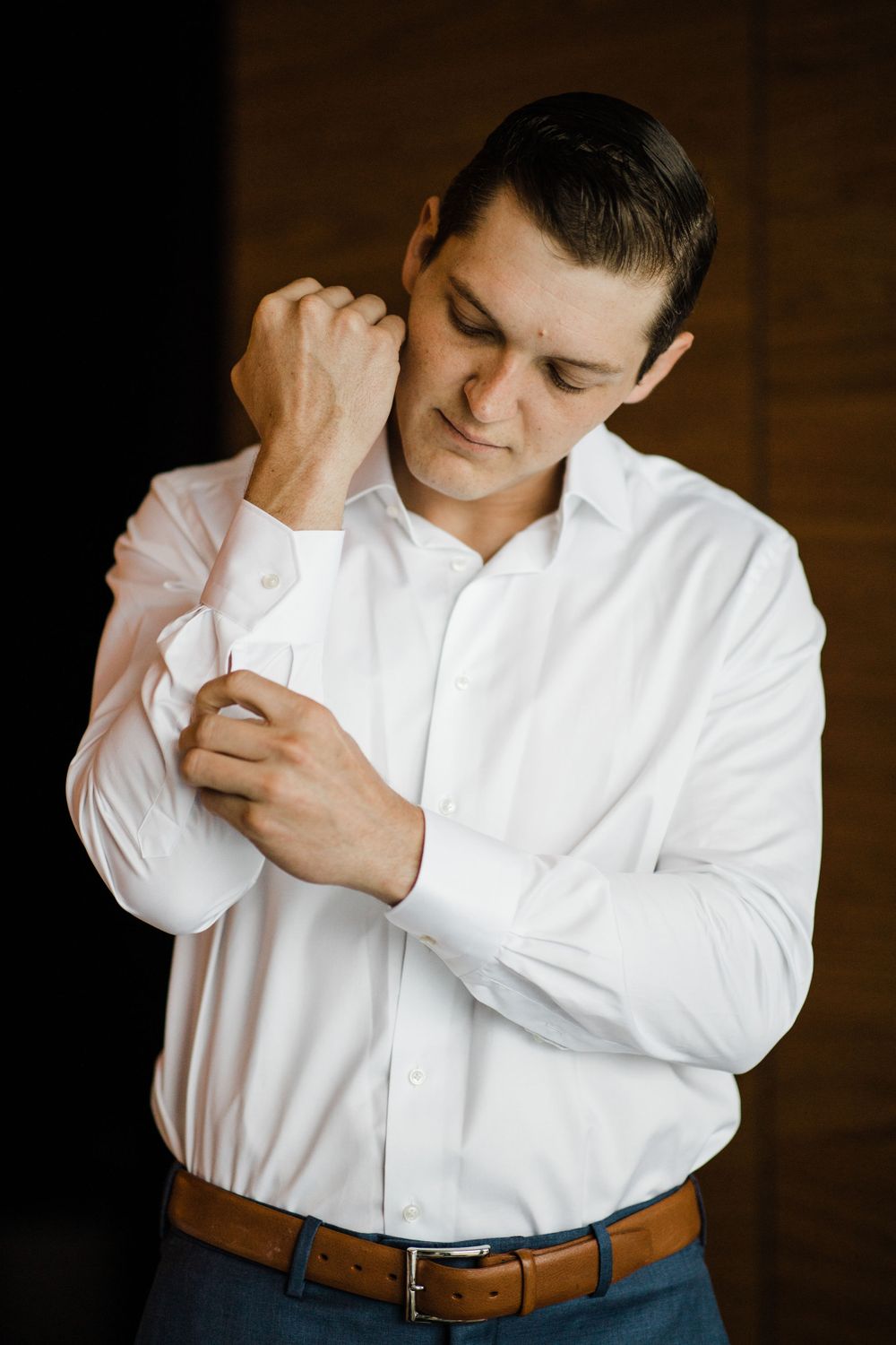 Person in white dress shirt and brown belt adjusting sleeve cuff.