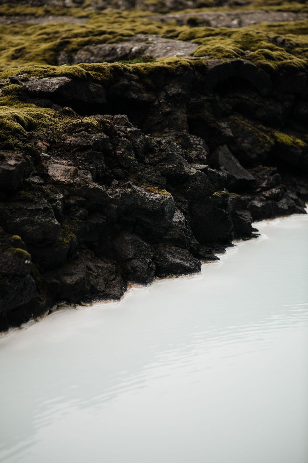 Mossy rocks meet calm water in minimalist nature landscape.