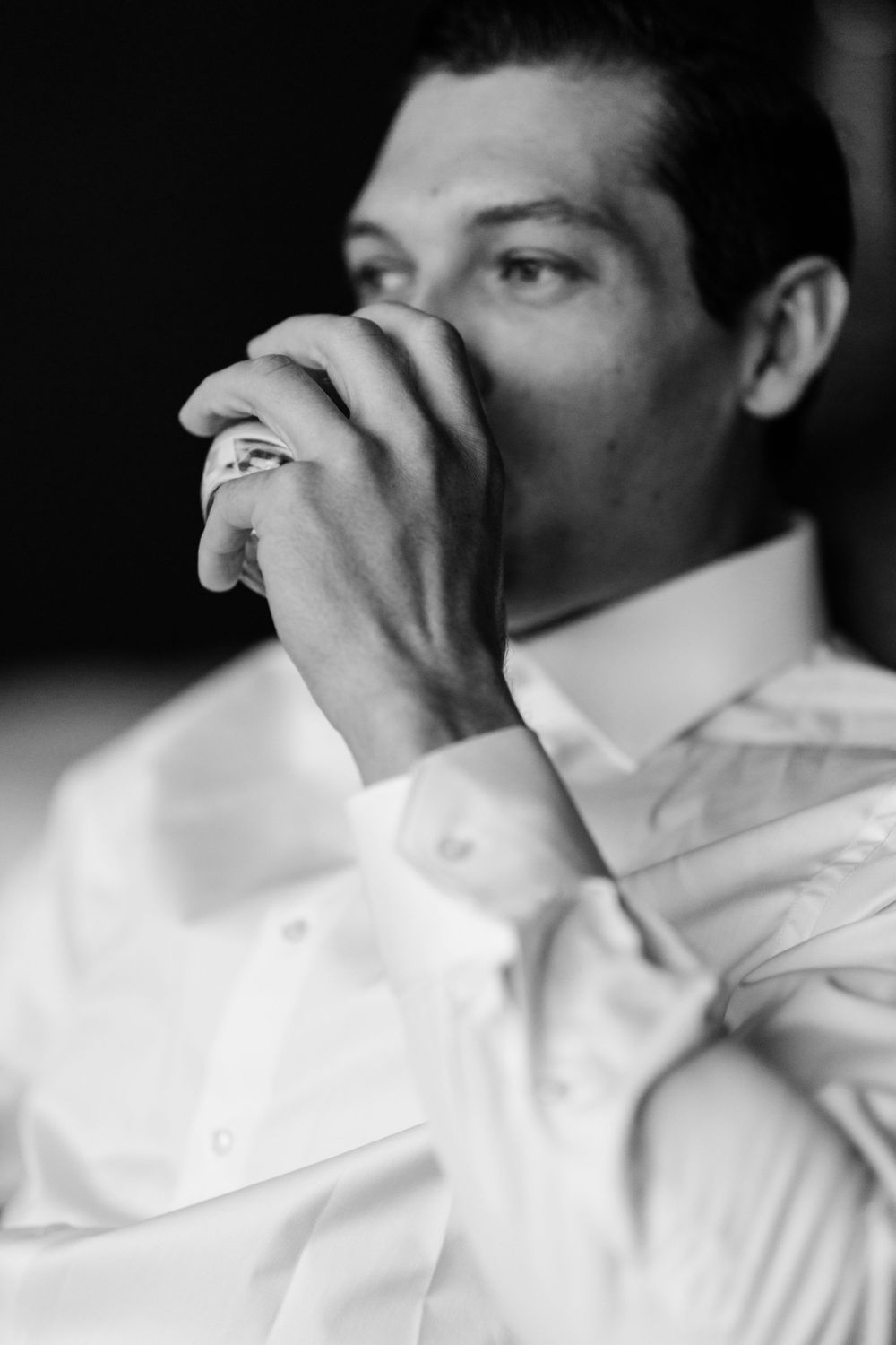 Close-up black and white portrait of person in white shirt covering face with hands.