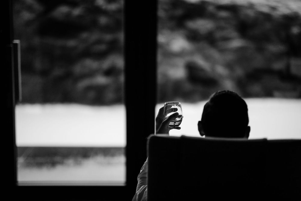 Silhouette of person holding drink while sitting by window.